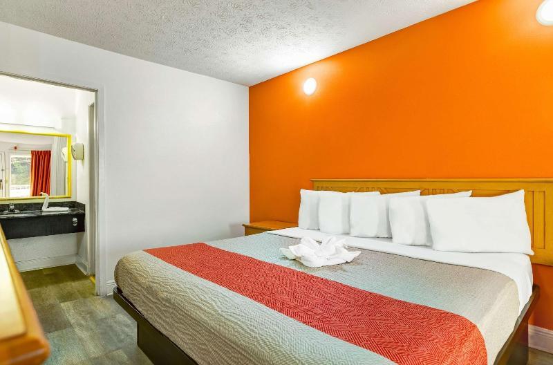 Three Queen Non-Smoking guest room with a bed against an orange accent wall and an open vanity area