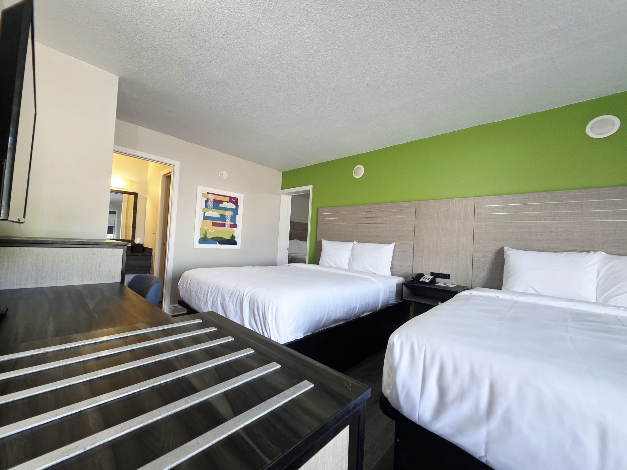 Three Queen Non-Smoking guest room with two queen beds against a green accent wall, a desk and an open bathroom doorway